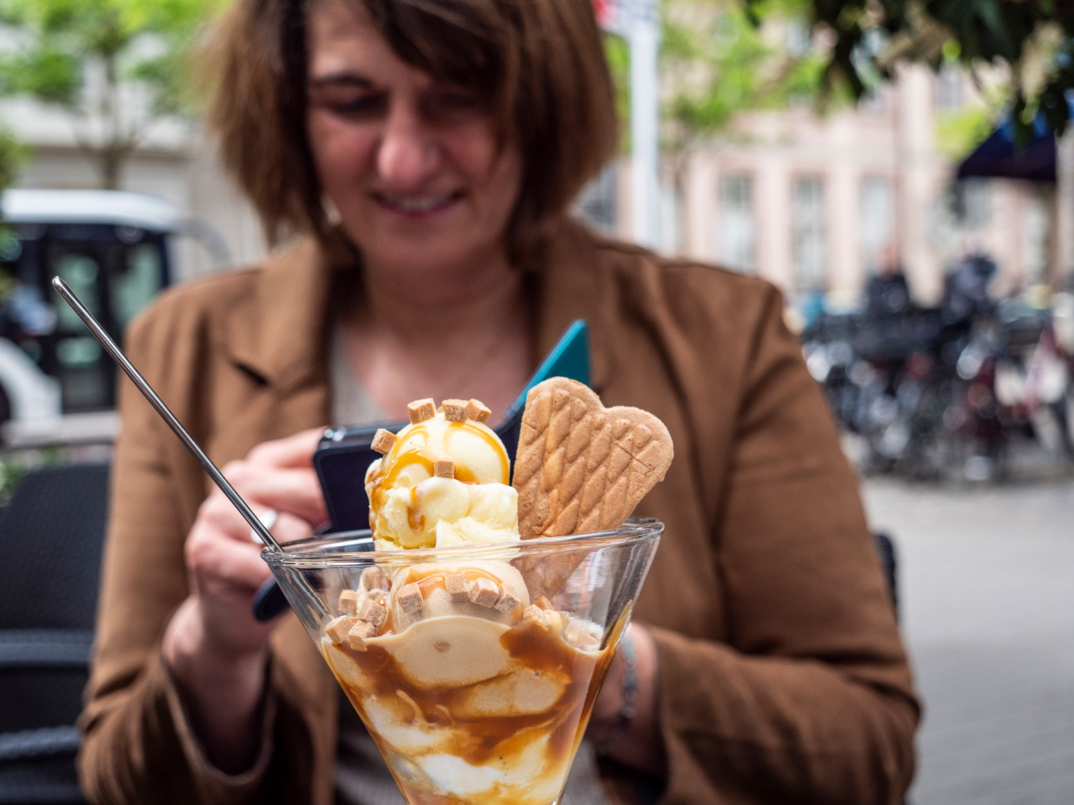 Auf das Smartphone blickende Frau. Im Vordergrund ihr Eisbecher