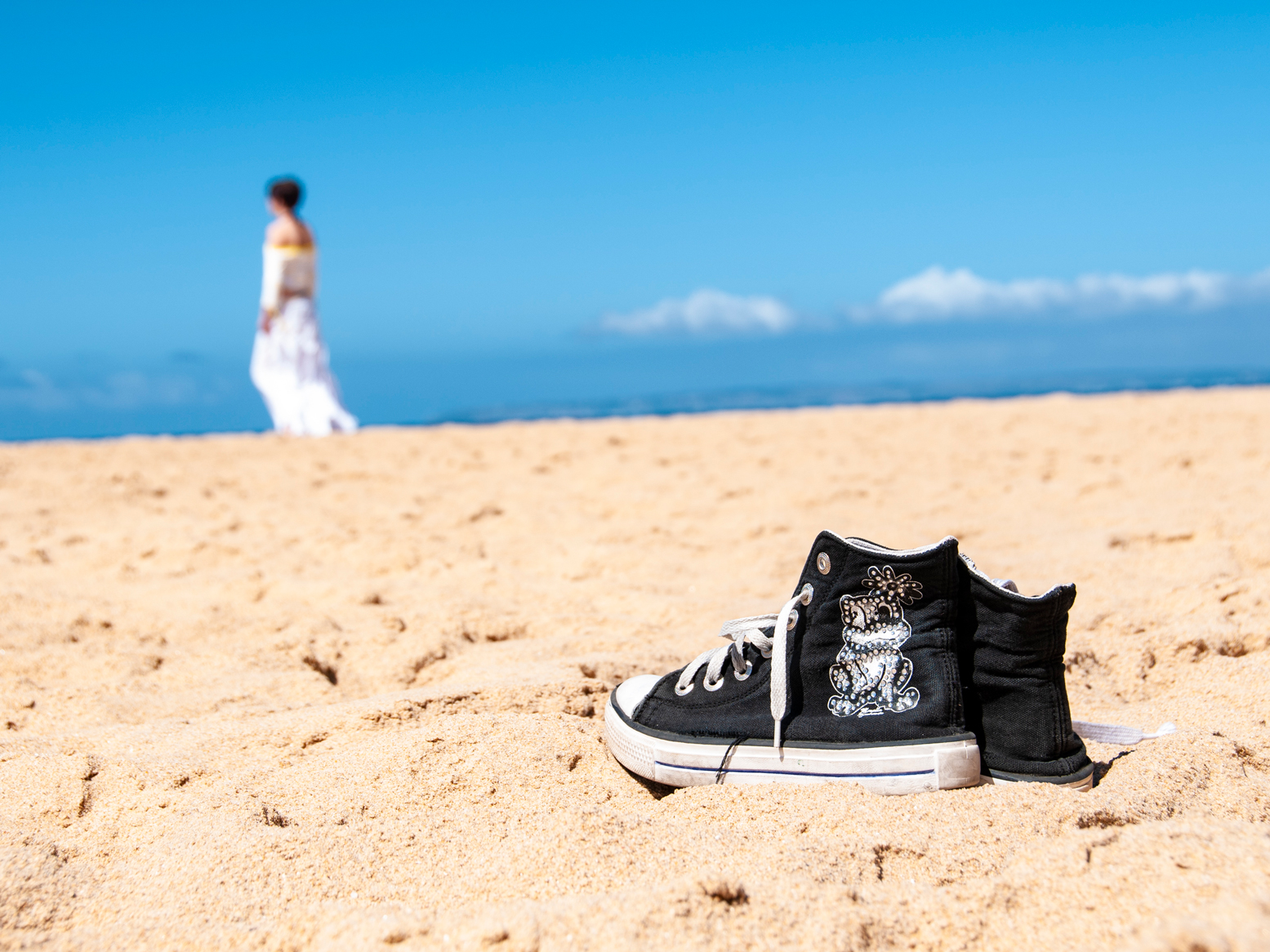 Frau spaziert den Strand entlang. Im Vorderung ihre Schuhe