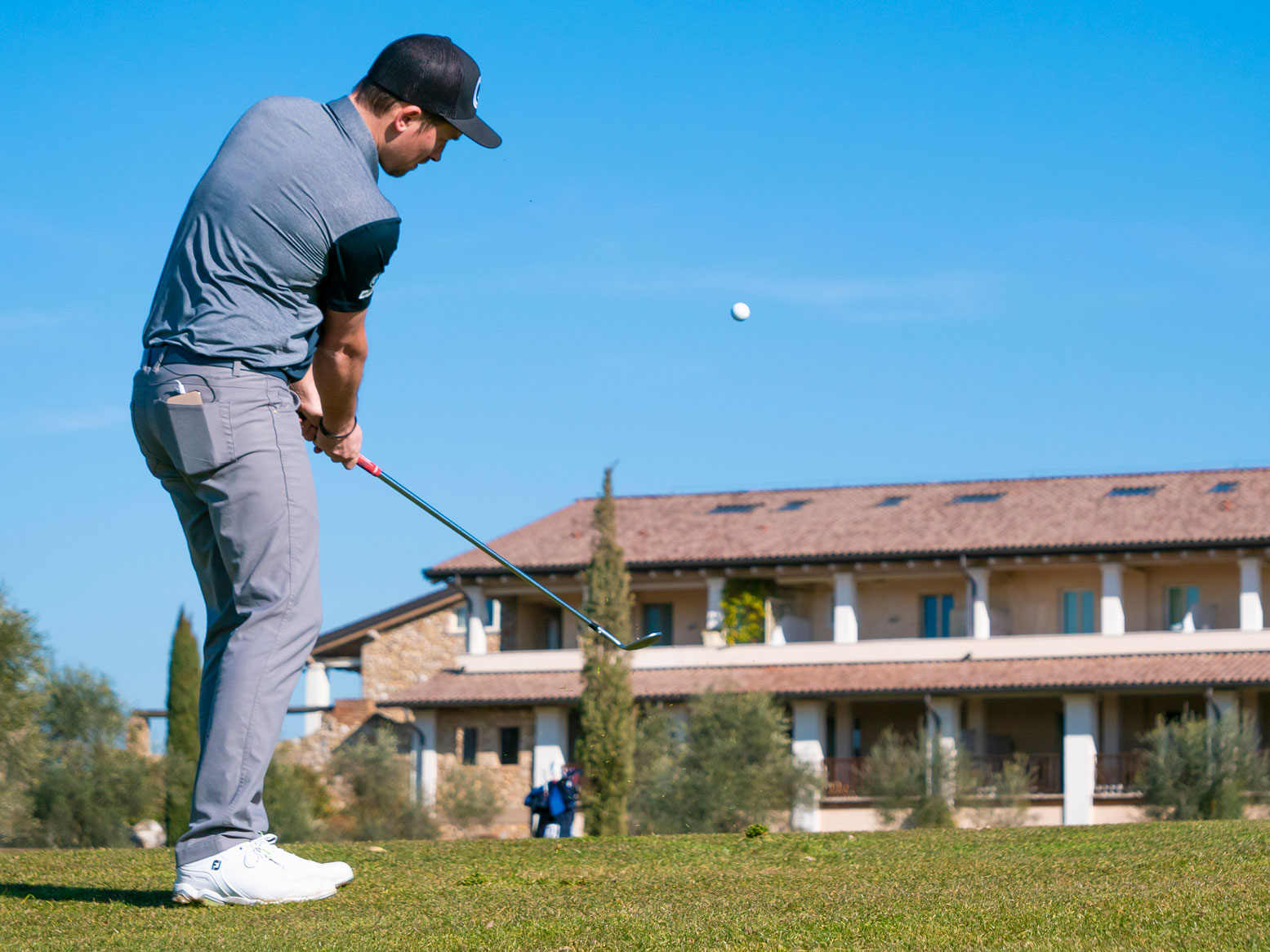 Golfpro beim Schlag mit dem Ball in der Luft. Die Perspektive ist vom Boden aus