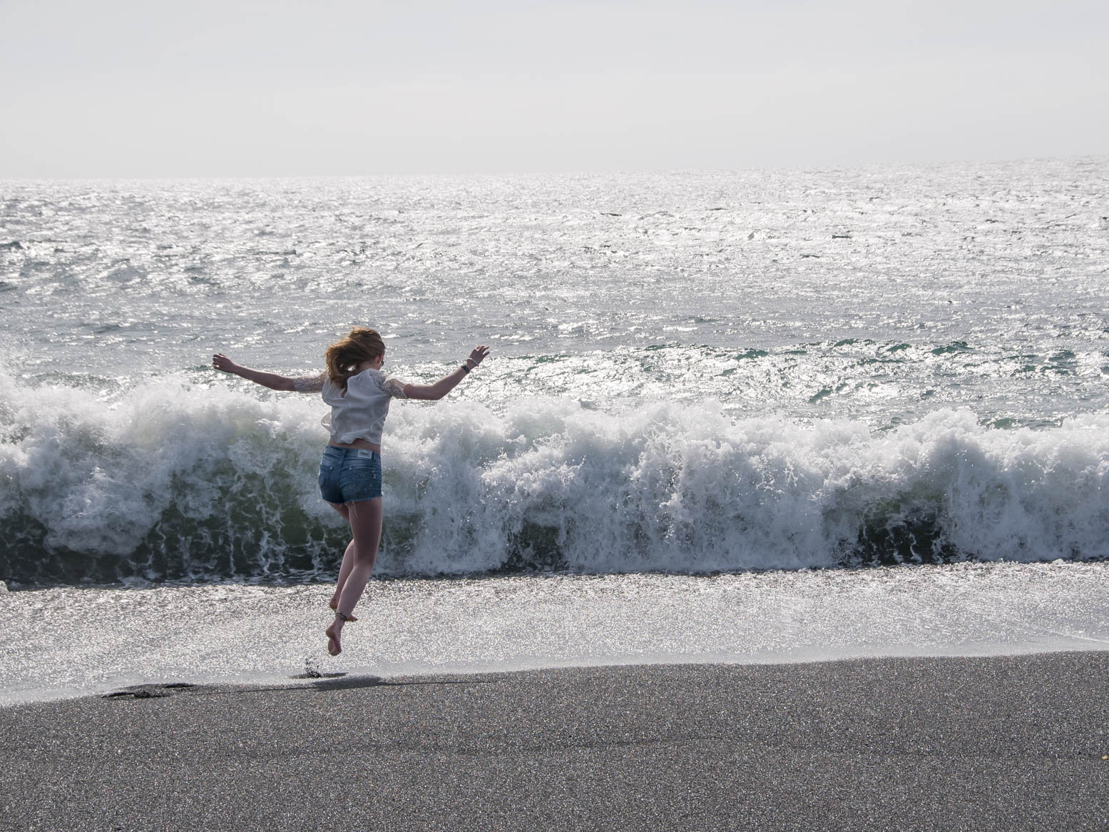 Junge Dame springt in Lanzarote vor den Wellen